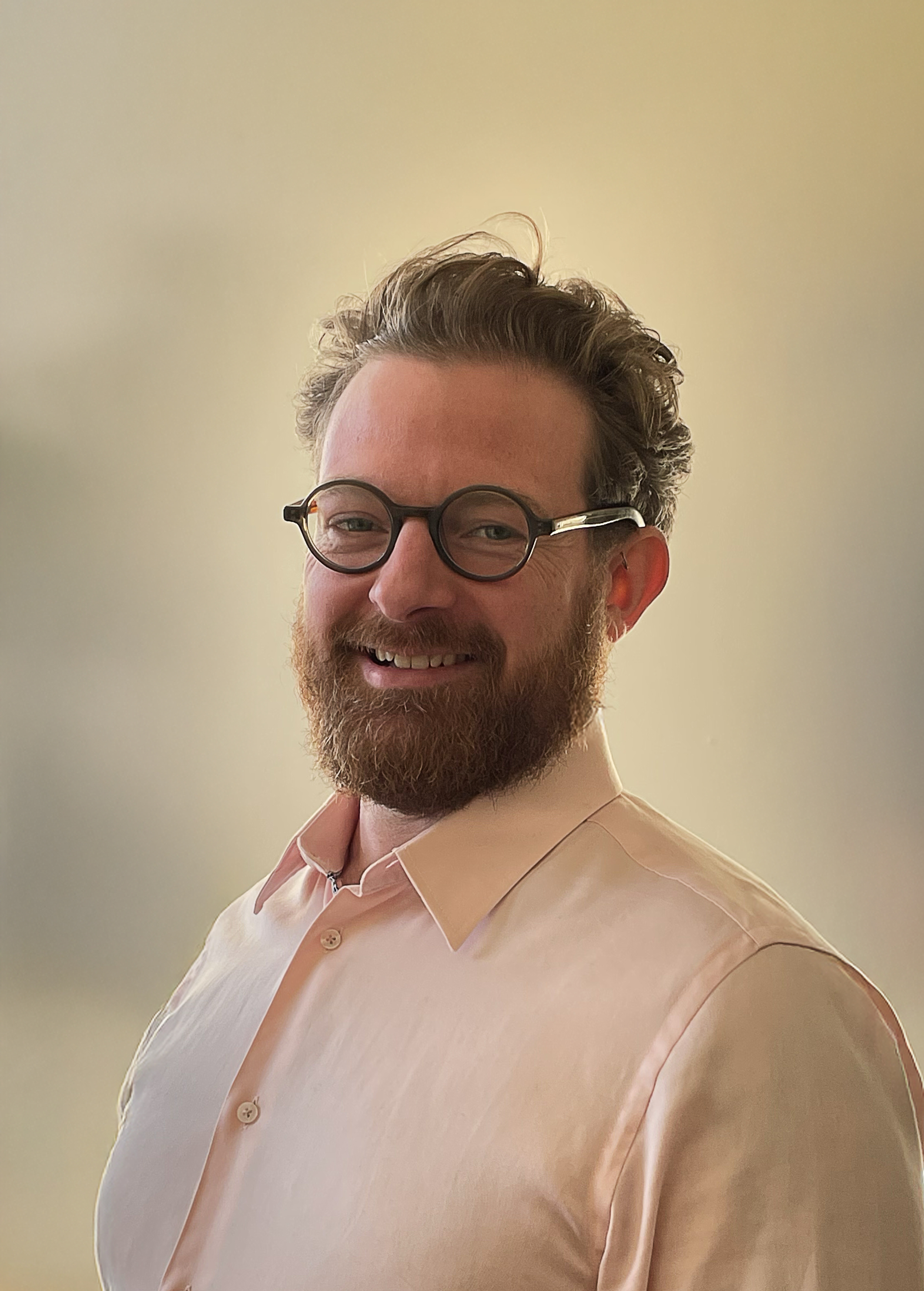 Portrait of Ian Wood wearing round glasses and a pale pink shirt.